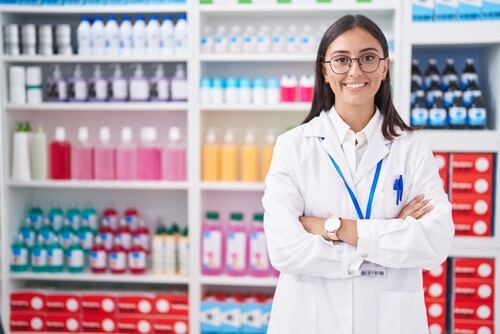 Mujer con bata de laboratorio de pie frente a estanterías llenas de frascos y materiales de investigación