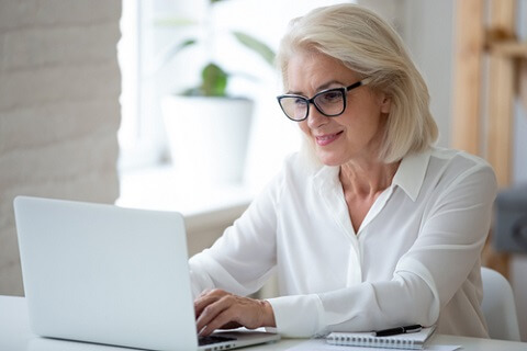 Mujer de mediana edad con gafas teletrabajando con su ordenador portátil