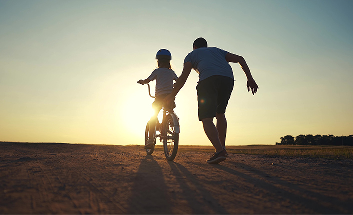Un padre ayuda a su hijo a montar en bicicleta en un descampado al atardecer
