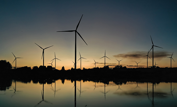 Parque eólico formado por varios aerogeneradores en un campo que hay detrás de un río al atardecer 