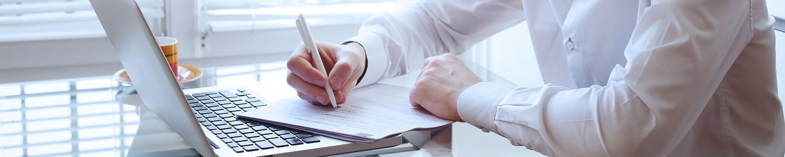 Hombre escribiendo con bolígrafo en un papel delante de un ordenador