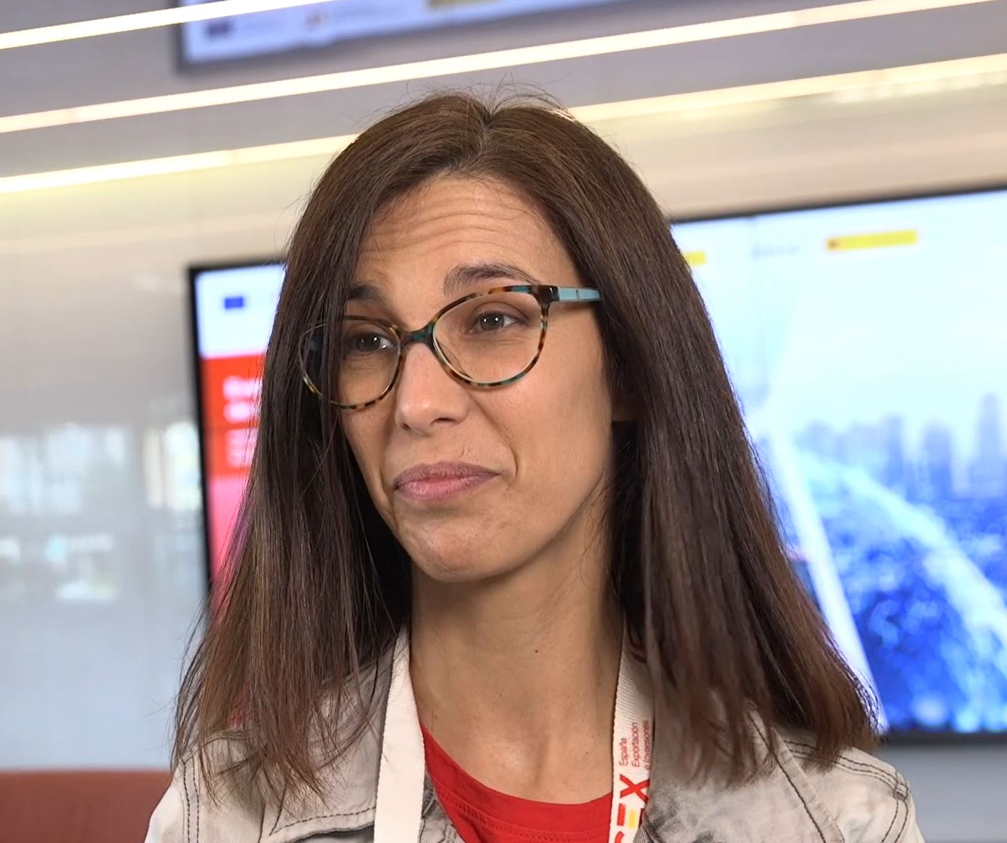 Mujer de pelo castaño con gafas y una chaqueta vaquera. Lleva al cuello una acreditación de ICEX