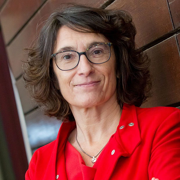 Mujer con cabello corto y ondulado, usa gafas. Viste chaqueta roja sobre blusa del mismo tono. Expresión tranquila.