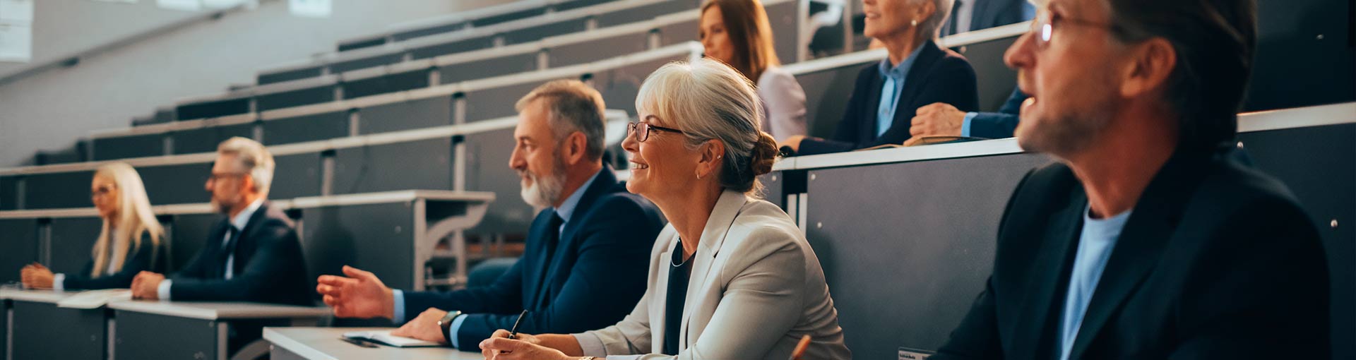 varias personas en un aula sonriendo donde se ve la cara de una persona con pelo blanco corto y gafas negras sonriendo
