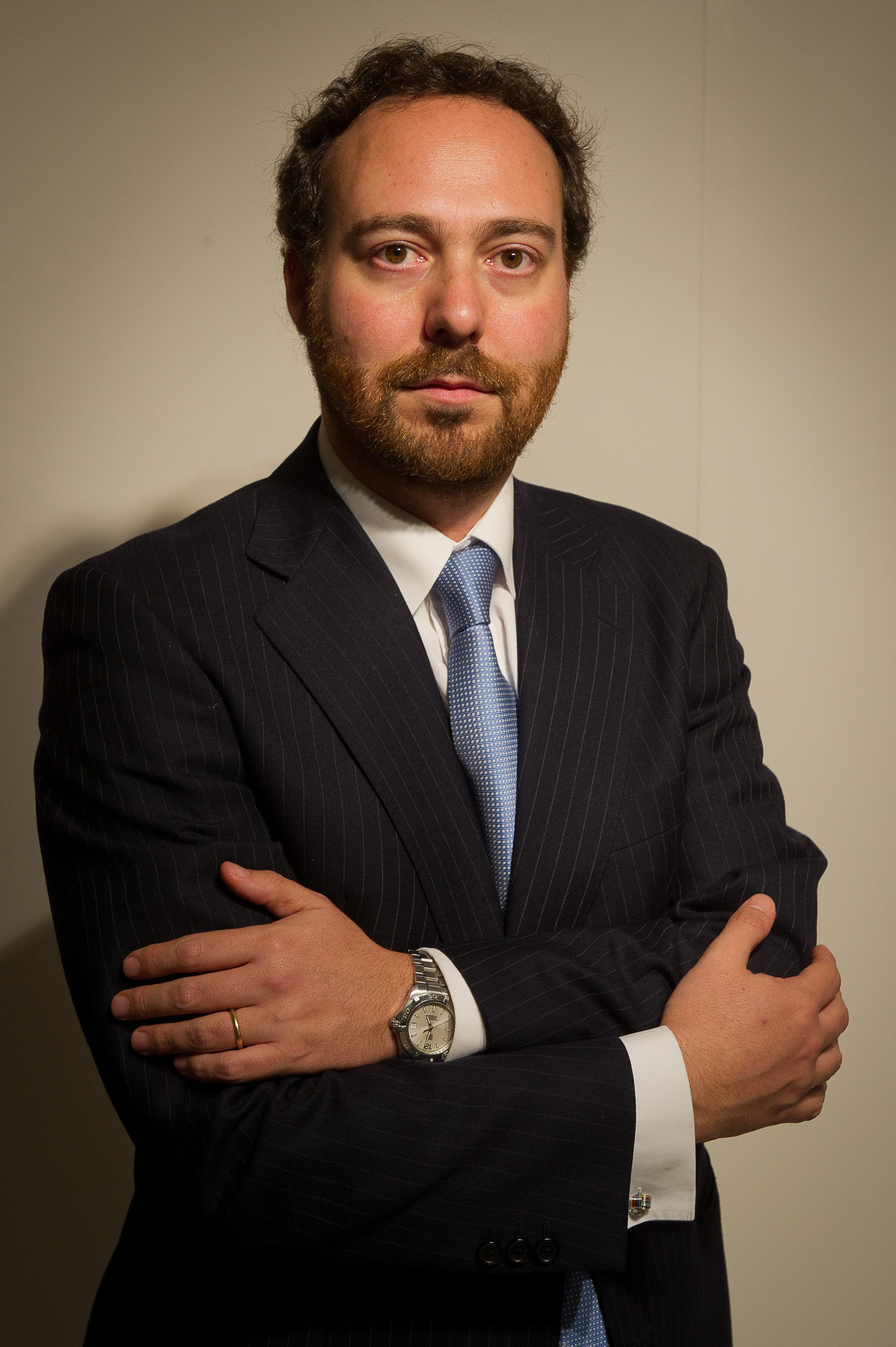 Plano americano de una persona con pelo corto, traje azul oscuro y corbata azul claro con los brazos cruzados