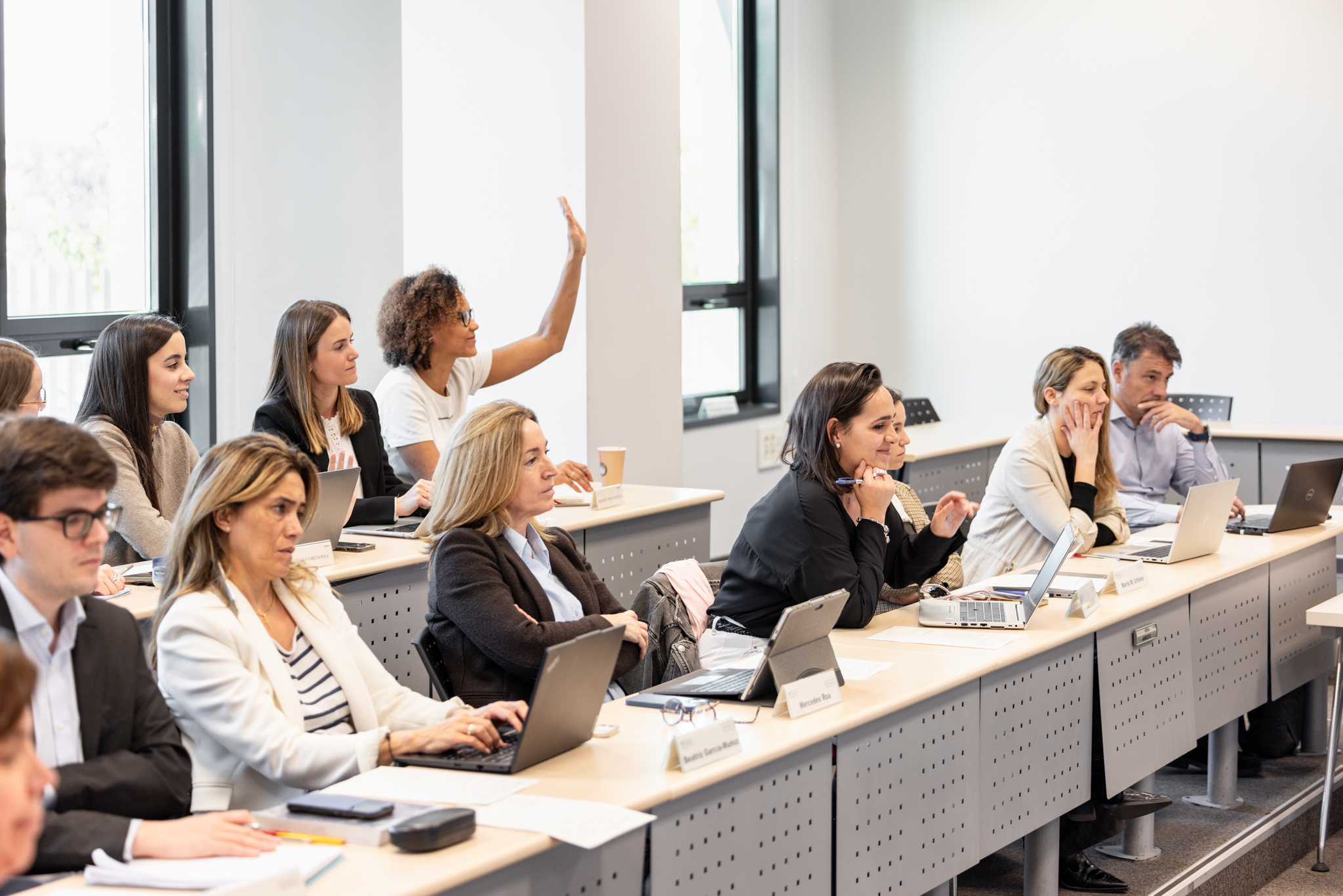 personas en dos filas de mesas con portátiles y una levanta una mano