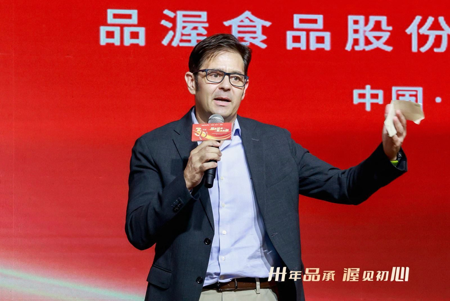 persona sujetando un micrófono con americana azul y dondo rojo con letras en chino