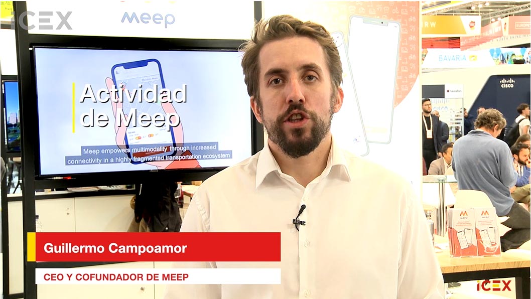 Hombre con barba vestido con camisa blanca, delante de un monitor que reproduce un vídeo promocional