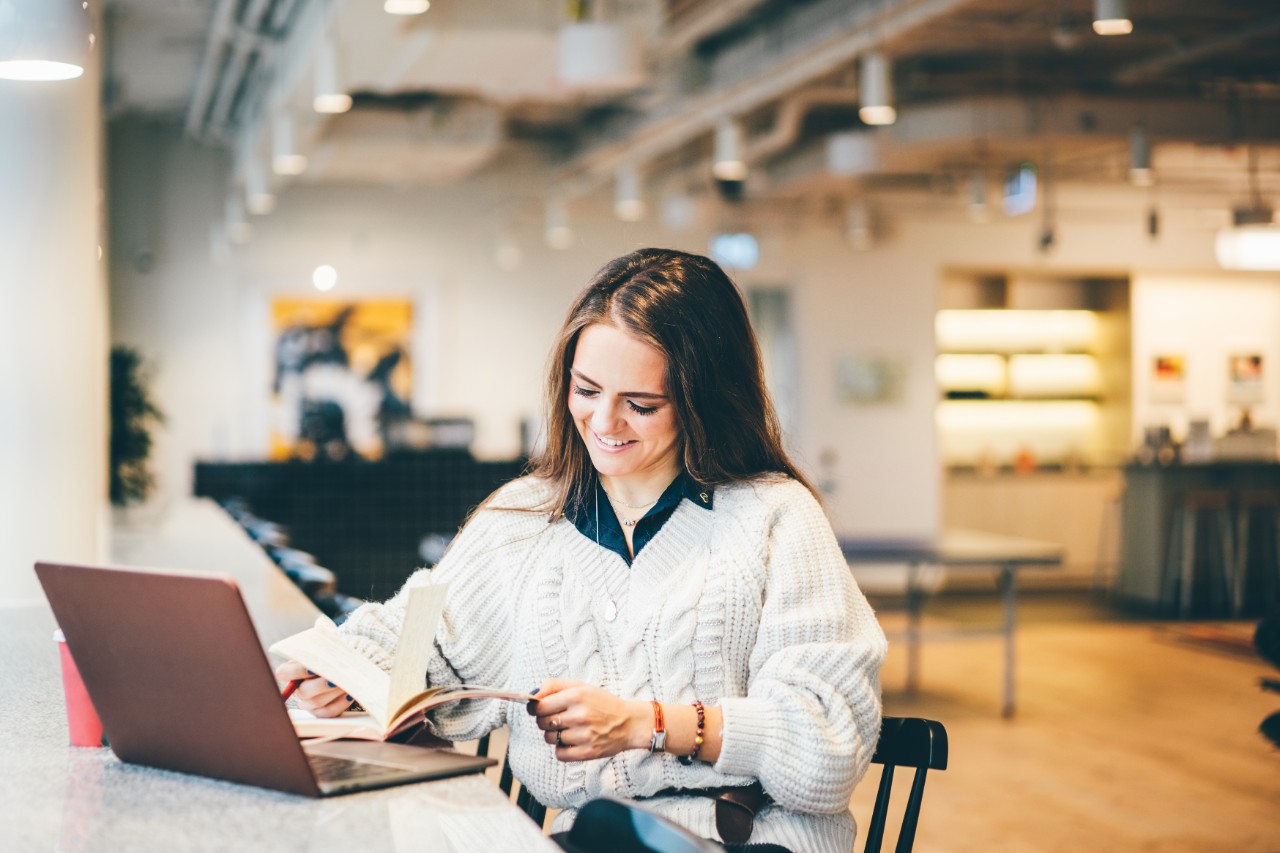 Businesswoman working on laptop in modern coworking. Young business woman sitting at the table and writing notes in notebook. Business concept.