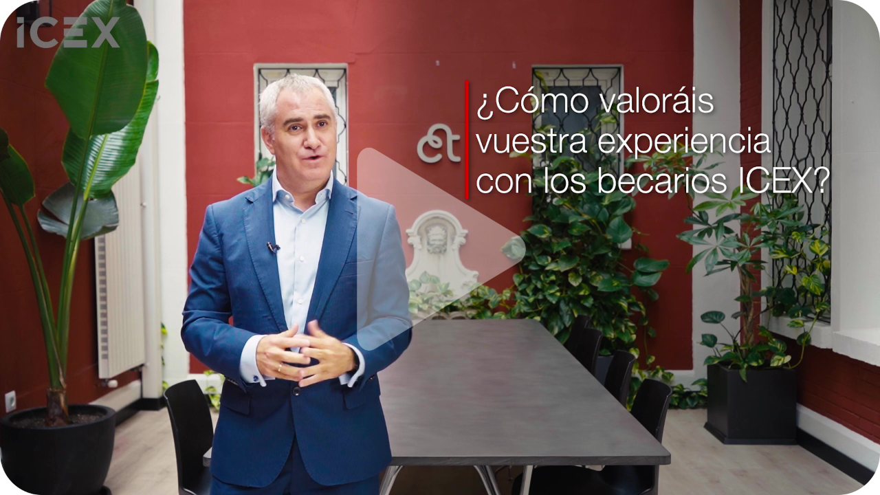 Plano americano de hombre con traje azul y pelo blanco sobre fondo rojo con plantas verdes