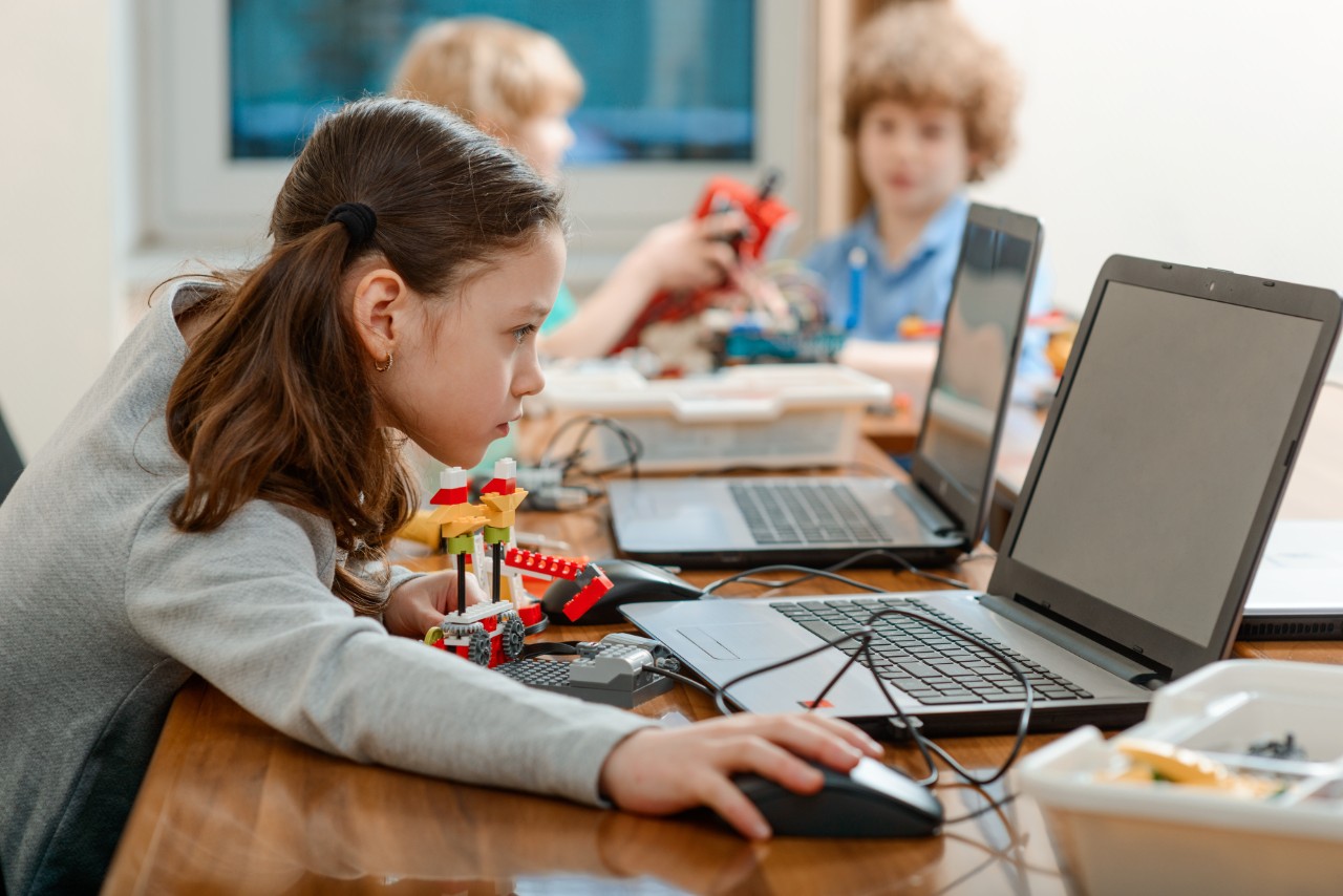 Girl using a laptop while assembling a robot from plastic bricks. STEM Education for kids.