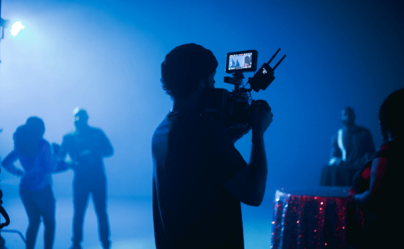 Un cámara graba una escena con varios actores sobre un fondo azul