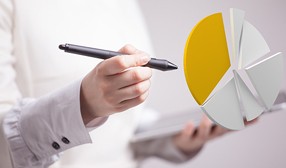 Una persona con camisa blanca sostiene un bolígrafo negro en una mano y una tablet en la otra. Además, sale una imagen de un gráfico en forma de queso partido por diversos fragmentos.