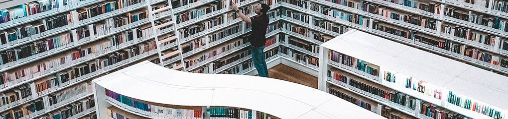 Un hombre coloca libros en una estantería blanca, junto a una escalera blanca, en una biblioteca