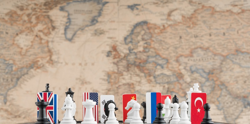 Country flag symbols on the chessboard with figures on the background of the political map of the world. Conceptual photo of a political game.