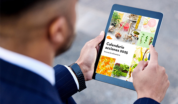 Un hombre con traje azul sujeta una tablet en la que se visualiza la portada del calendario de actividades para foodtech