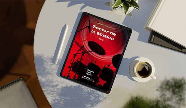 Sobre una mesa blanca hay un bolígrafo blanco, una tablet donde se visualiza la portada del calendario ICEX del sector de la música y una taza blanca con café.