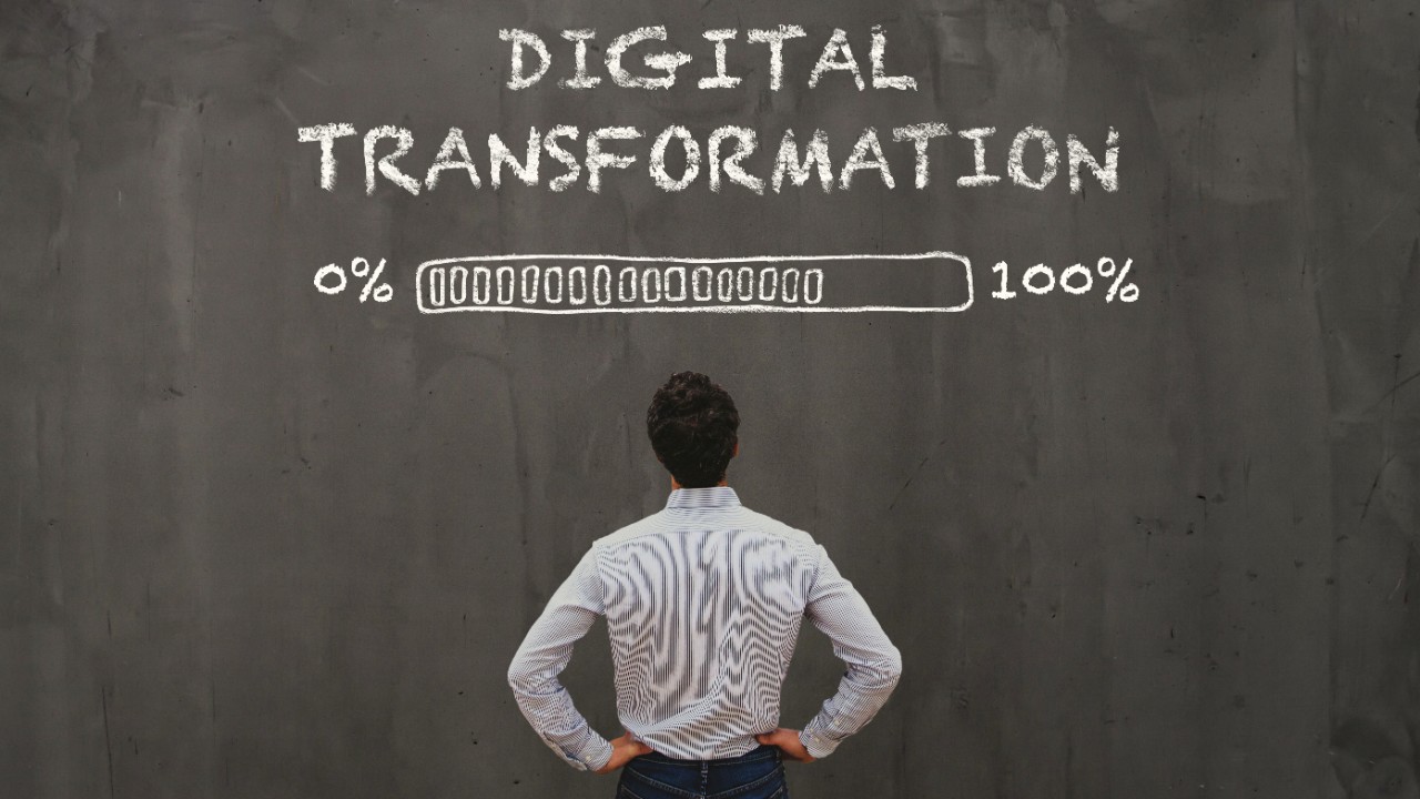 Un hombre lee el letrero Digital Transformation y un gráfico de carga del 0% al 100% en una pizarra