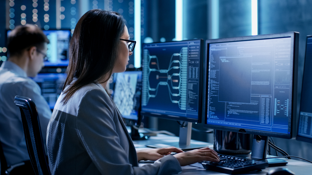 Over The Shoulder Footage of Female IT Engineer Working in Monitoring Room. She Works with Multiple Displays.