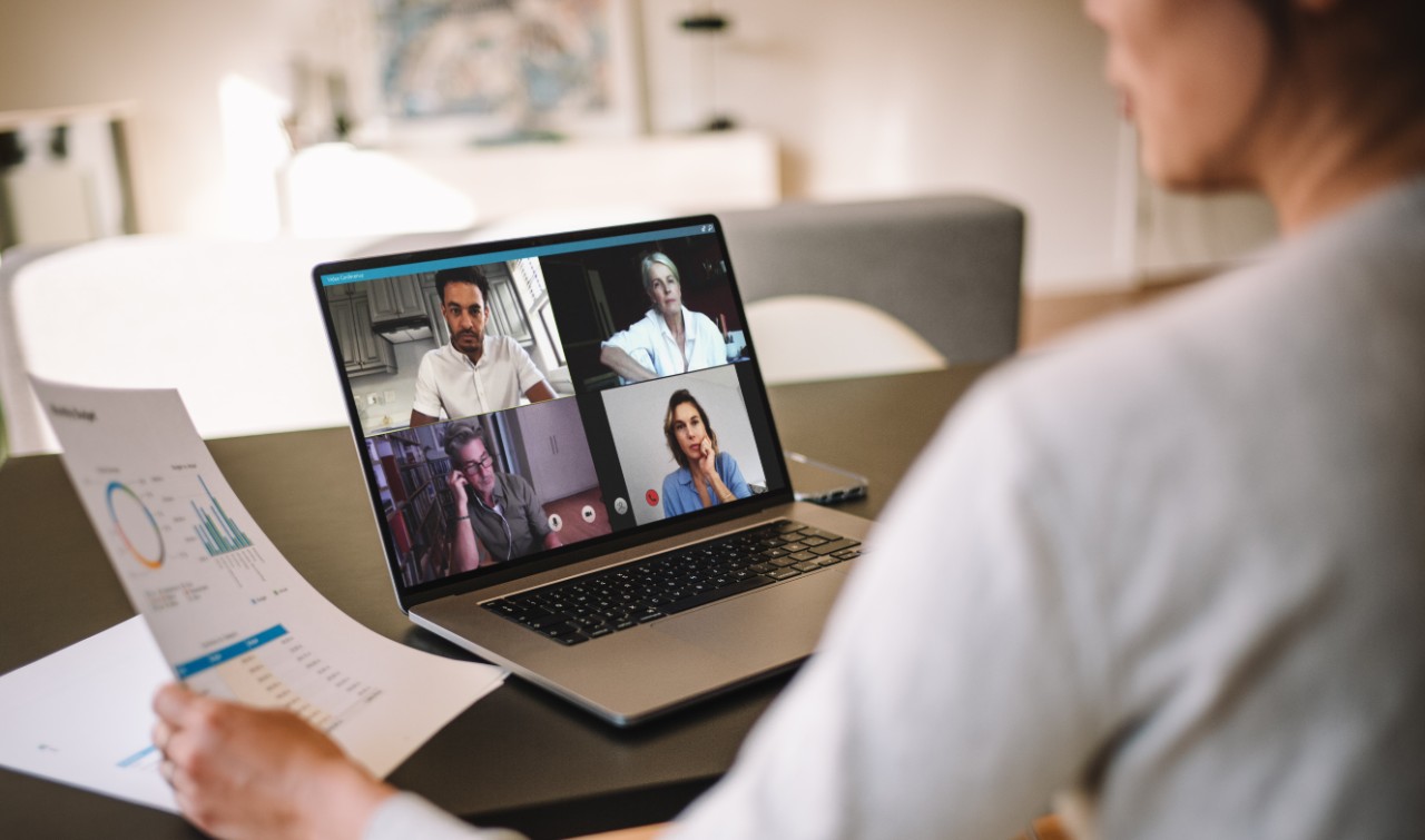 Office colleagues having a video call to discuss few financial reports. Business people working from home having a video conference. Over the shoulder view.