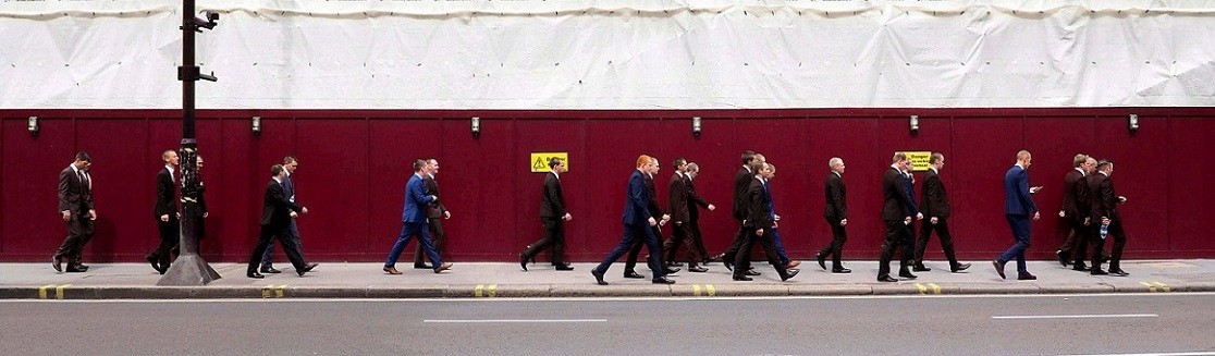 Un grupo de personas vestidas con traje camina frente a una valla roja. Siguen los pasos para vender en Reino Unido