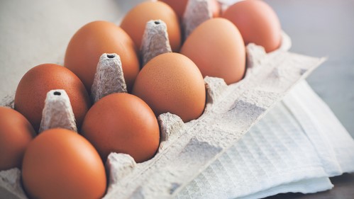 Un recipiente de cartón grisáceo (o huevera) con una decena de huevos anaranjados