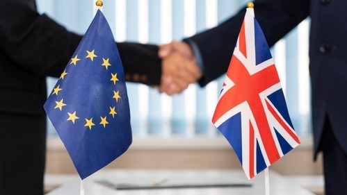 Dos personas estrechándose la mano, con las dos banderas de la Unión Europea y Reino Unido. 