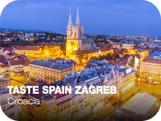 Taste Spain Zagreb. Croacia. Desde lo alto se ven varios edificios y una catedral de la ciudad, todos ellos iluminados por intensas las luces amarillas de las farolas de las calles.