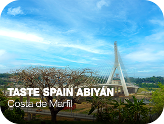 Taste Spain Abiyán. Costa de Marfil. Varios árboles, una carretera, y detrás, un puente blanco con arcos
