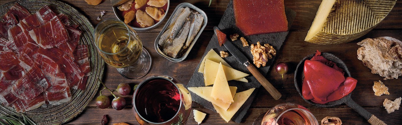 Cotillón que incluye un plato con jamón ibérico, quesos, copas de vino tinto y blanco, pan, pimientos, pescado en conserva...etc.